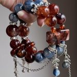 1. Handmade crystal bracelet with blue kyanite and red healer quartz beads, silver butterfly and bell charms, on clear acrylic stand