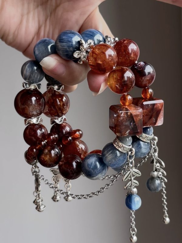 1. Handmade crystal bracelet with blue kyanite and red healer quartz beads, silver butterfly and bell charms, on clear acrylic stand